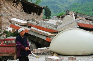 倒壊した建物の前に立ち尽くす女性 Photo: Liu Liangchuan/Mercy Corps